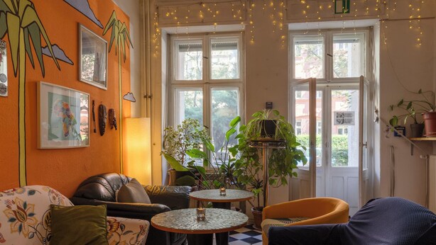 A cozy room with a checkered floor, a sofa, a chair, and a small table with a candle. - BackpackerBerlin (Berlin)