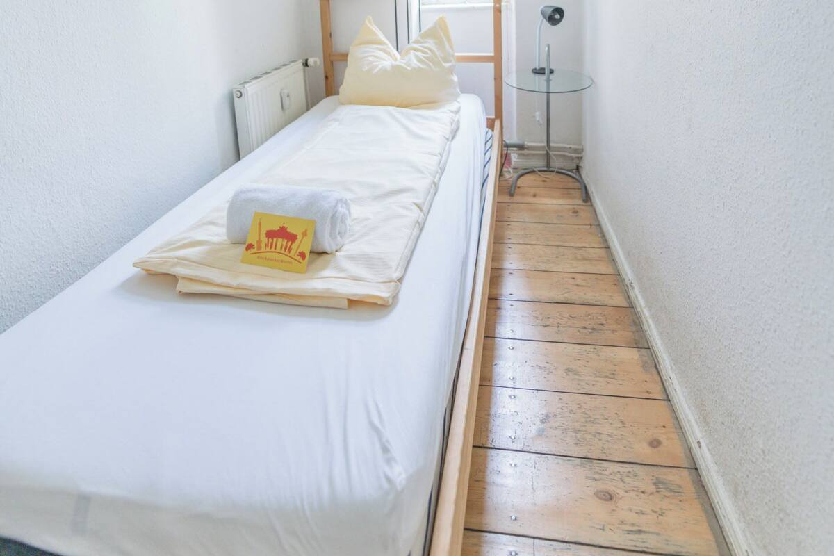 A narrow room with a single bed, a small table, and a window.