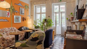 A cozy room with a checkered floor, a sofa, a chair, a small table, and a bookshelf. There are windows with curtains and a plant on a stand. - BackpackerBerlin (Berlin)