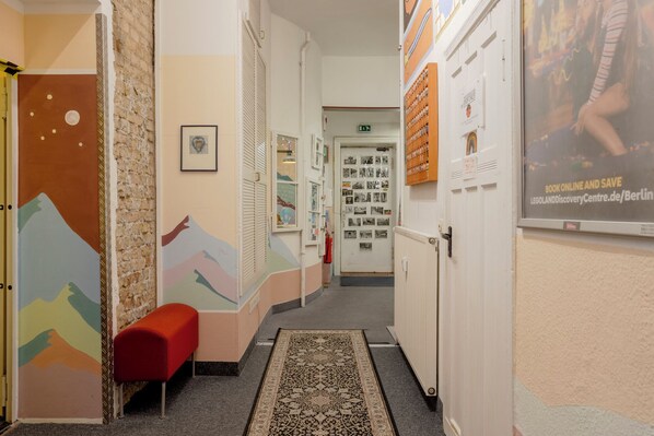 A hallway with a red bench, a patterned rug, and a door with photos on the wall. - BackpackerBerlin (Berlin)