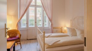 A bedroom with a bed, a chair, a window with curtains, and a radiator. - BackpackerBerlin (Berlin)