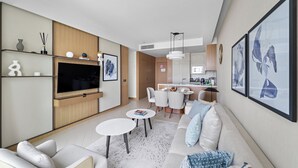 A modern living room with a flat-screen TV, a sofa, a dining table, and a kitchen area in the background. - 2BR Pool with Burj Khalifa View (Dubai)