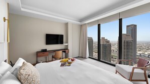 A modern hotel room with a large bed, a desk, a chair, a TV, and a view of city buildings. - 2BR Pool with Burj Khalifa View (Dubai)