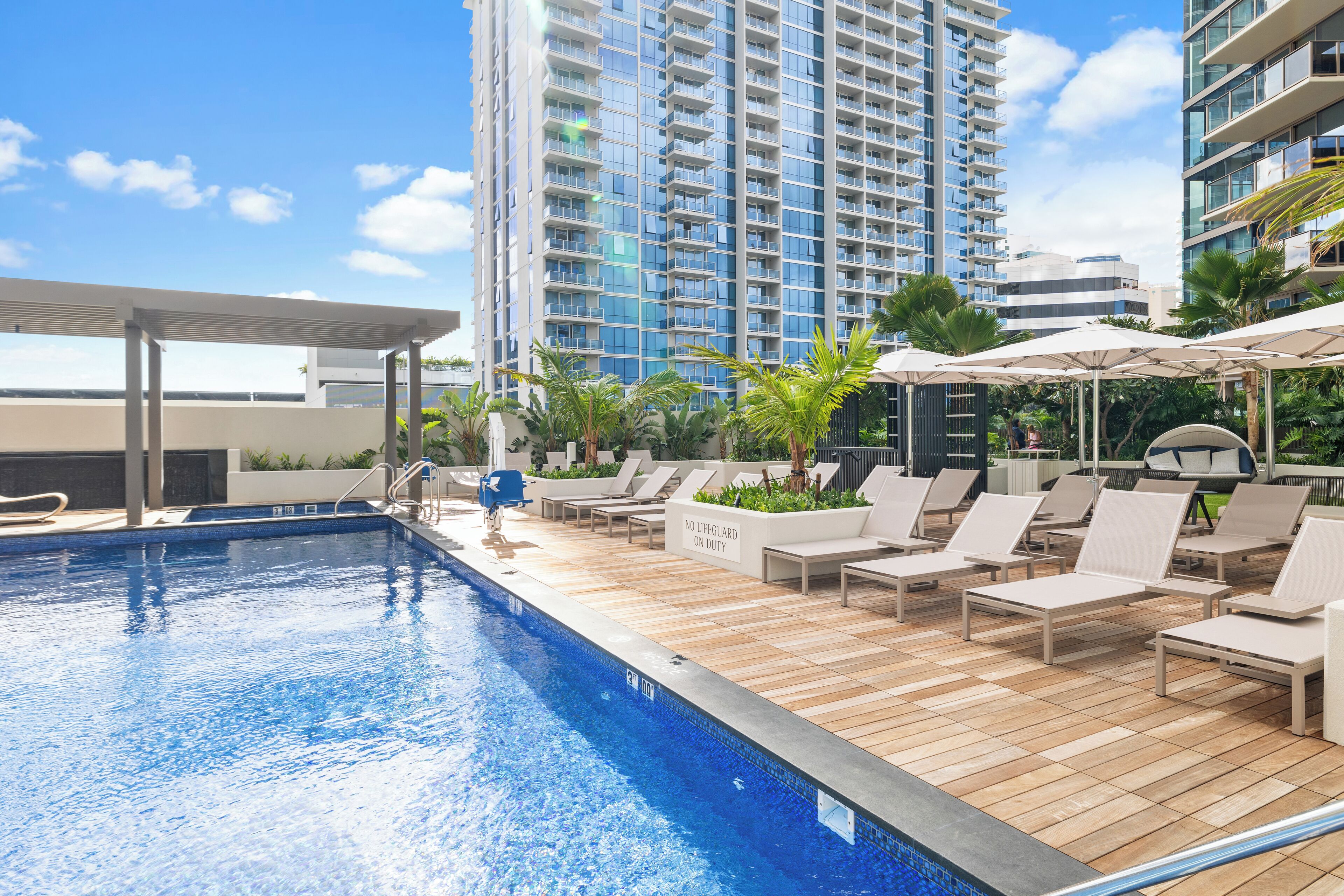 A rooftop pool area with lounge chairs and umbrellas, surrounded by tall buildings.