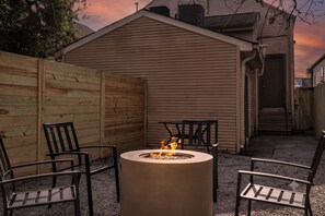 A circular fire pit with chairs around it, set against a wooden fence and a house with a sloped roof. - Victorian duplex near Downtown & Superdome. 1 mile to FQ, yard with fire pit & BBQ. (New Orleans)