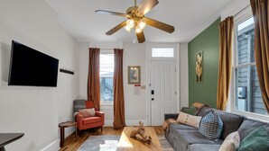 Ein Wohnzimmer mit Deckenventilator, Flachbildfernseher, einem roten Sofa, einem grauen Sofa und einem Couchtisch aus Holz.
