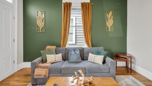 Ein Wohnzimmer mit grauem Sofa, einem Holztisch und einem Fenster mit Vorhängen.