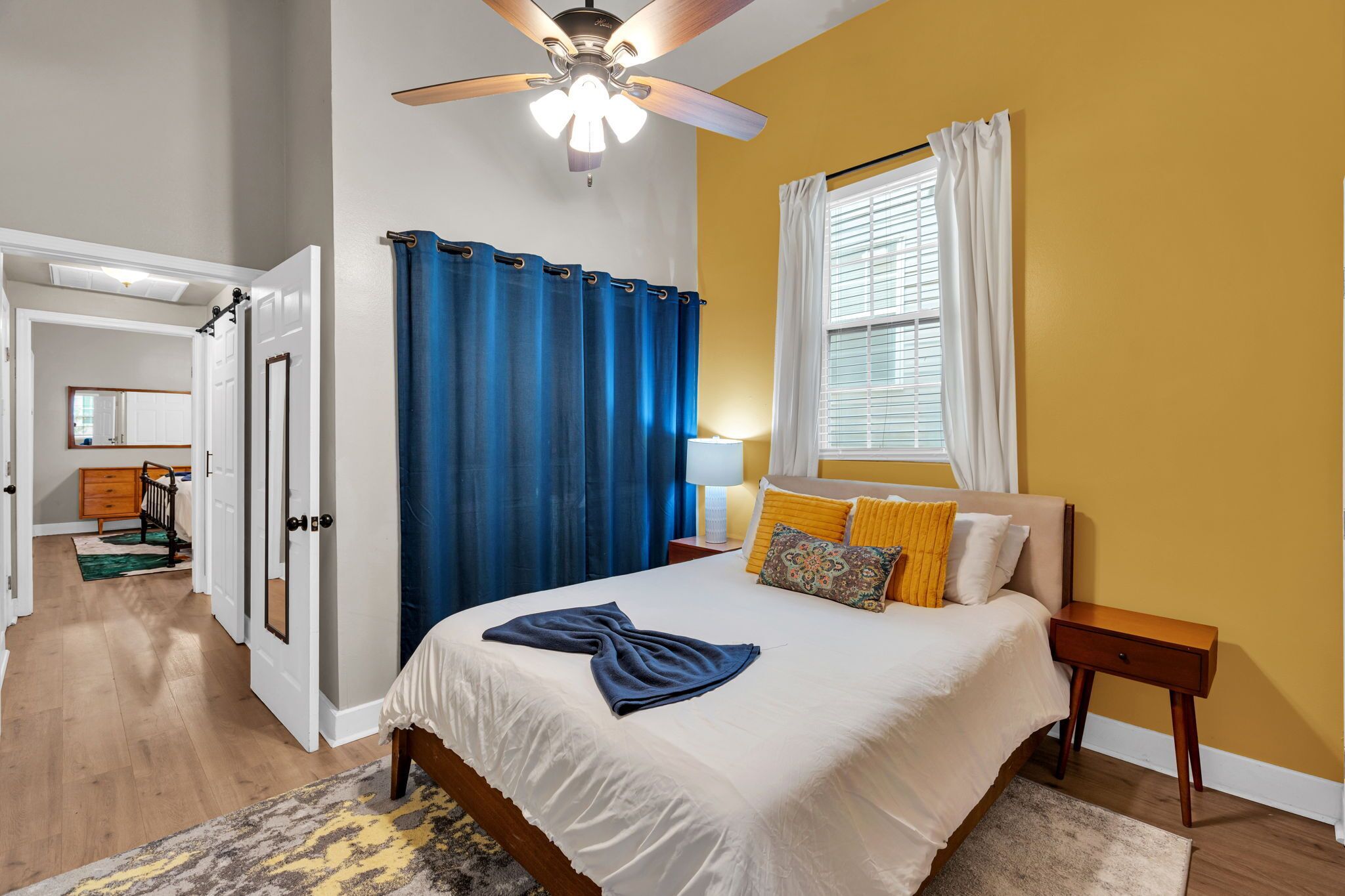 Une chambre à coucher avec un lit, un ventilateur de plafond, une fenêtre avec des rideaux et une table de chevet.