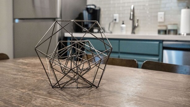 Une sculpture métallique aux formes géométriques, posée sur une table en bois dans une cuisine moderne aux armoires de couleur turquoise et aux appareils en acier inoxydable.