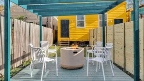 Une terrasse avec un foyer et des chaises blanches, le tout abrité par une pergola en bois.