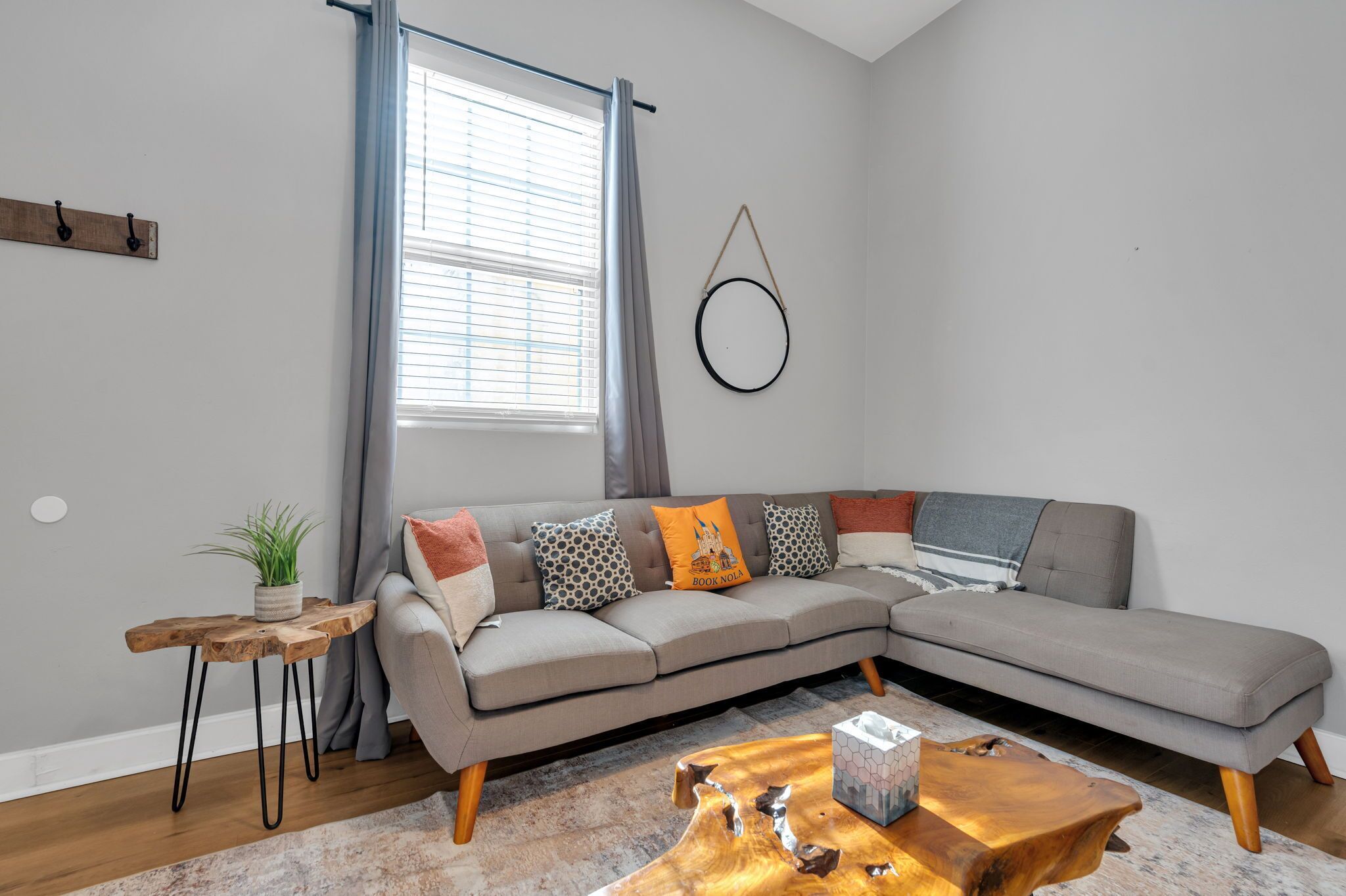 Ein modernes Wohnzimmer mit einem grauen Ecksofa, einem Holztisch und einem kleinen Beistelltisch mit Pflanze.