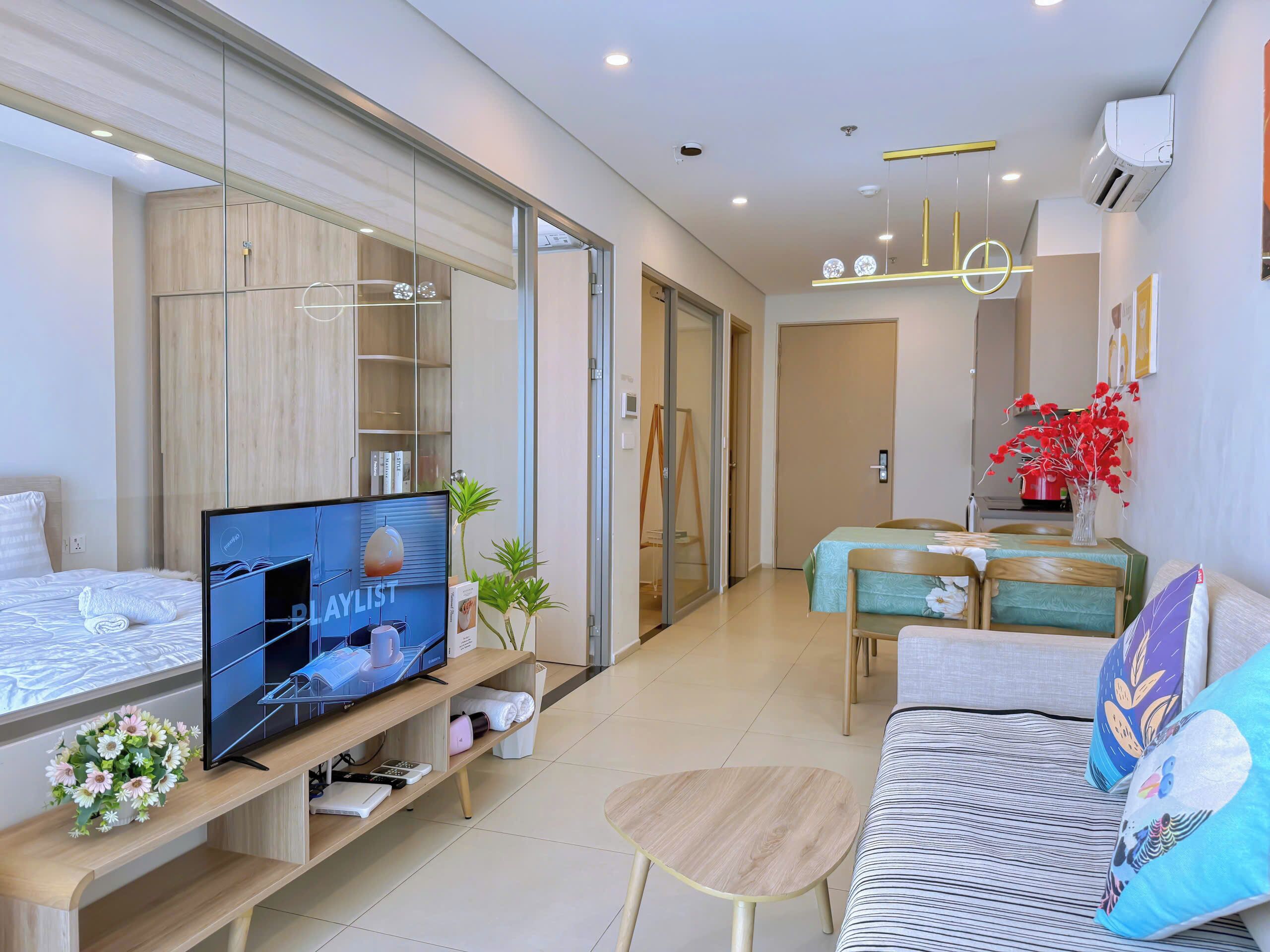 A modern hotel room with a large flat-screen TV, a sofa, a small round table, and a dining area with a table and chairs.