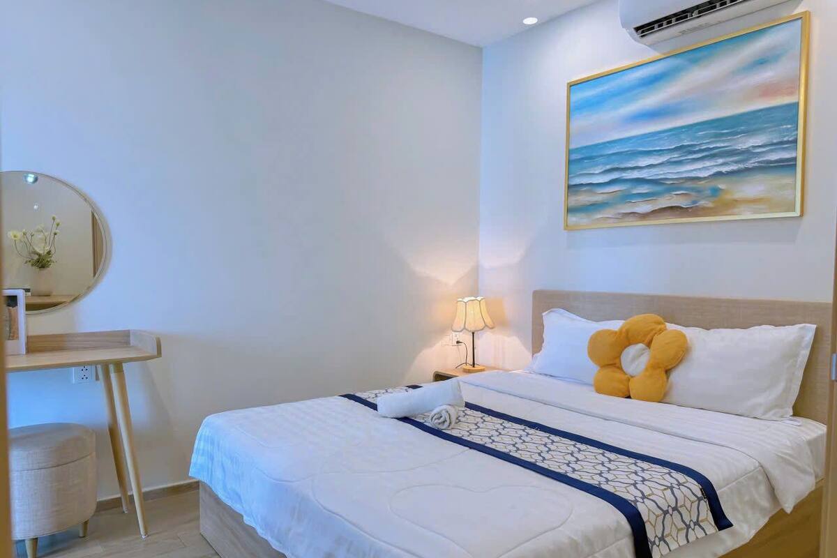 Ein Hotelzimmer mit einem Bett, einem Schreibtisch, einem Stuhl, einer Lampe und einem Meeresbild an der Wand.