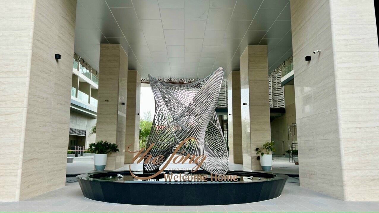 Un bâtiment moderne doté d’un élément architectural unique en son centre, entouré d’un bassin circulaire et de plantes en pot.