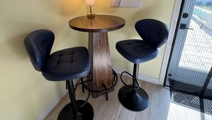 A corner room with a wooden table and two black chairs, a lamp, and a palm tree painting on the wall.