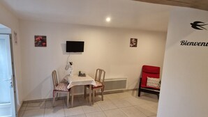 Une petite pièce avec une table et deux chaises, dont une chaise rouge, un téléviseur fixé au mur et une pancarte indiquant « Bienvenue ».