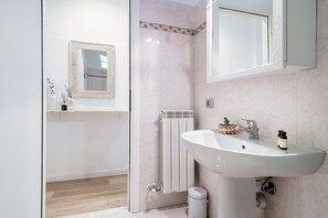 Un bagno con lavandino bianco, uno specchio, un termosifone e un cestino per i rifiuti.