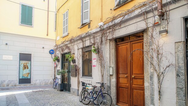 A cobblestone street with a yellow building featuring a wooden door and a sign with the number 44. - Il Nido tra le Mura (Como)