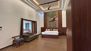 A modern bedroom with a large bed, a seating area, and a wardrobe. - Earth Home Pilibhit (Puranpur)