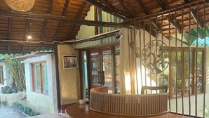 A wooden reception desk with a circular design, a high ceiling with exposed beams, and a view of the outdoors through large windows. - Earth Home Pilibhit (Puranpur)