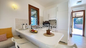 Una cocina moderna con armarios blancos, una isla central con taburetes, horno empotrado y ventana con vistas al verdor.