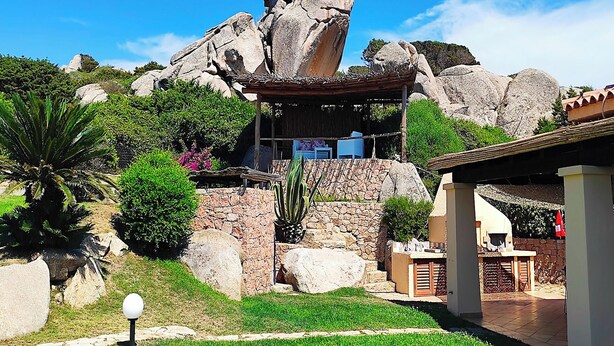 Un jardín con una formación rocosa, un pabellón y un muro de piedra.