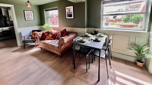 A cozy living room with a sofa, dining table set for four, and a window with a view of a garden. - Large Period Property On The Edge Of City Centre. (Worcester)