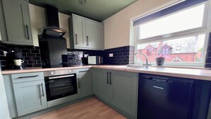 A modern kitchen with grey cabinets, a black dishwasher, and a window with a view of a red brick house. - Large Period Property On The Edge Of City Centre. (Worcester)