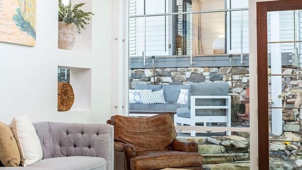 Ein modernes Wohnzimmer mit einem grauen Sofa, einem Holztisch und einem braunen Ledersessel. Ein großes Fenster bietet Blick ins Freie.
