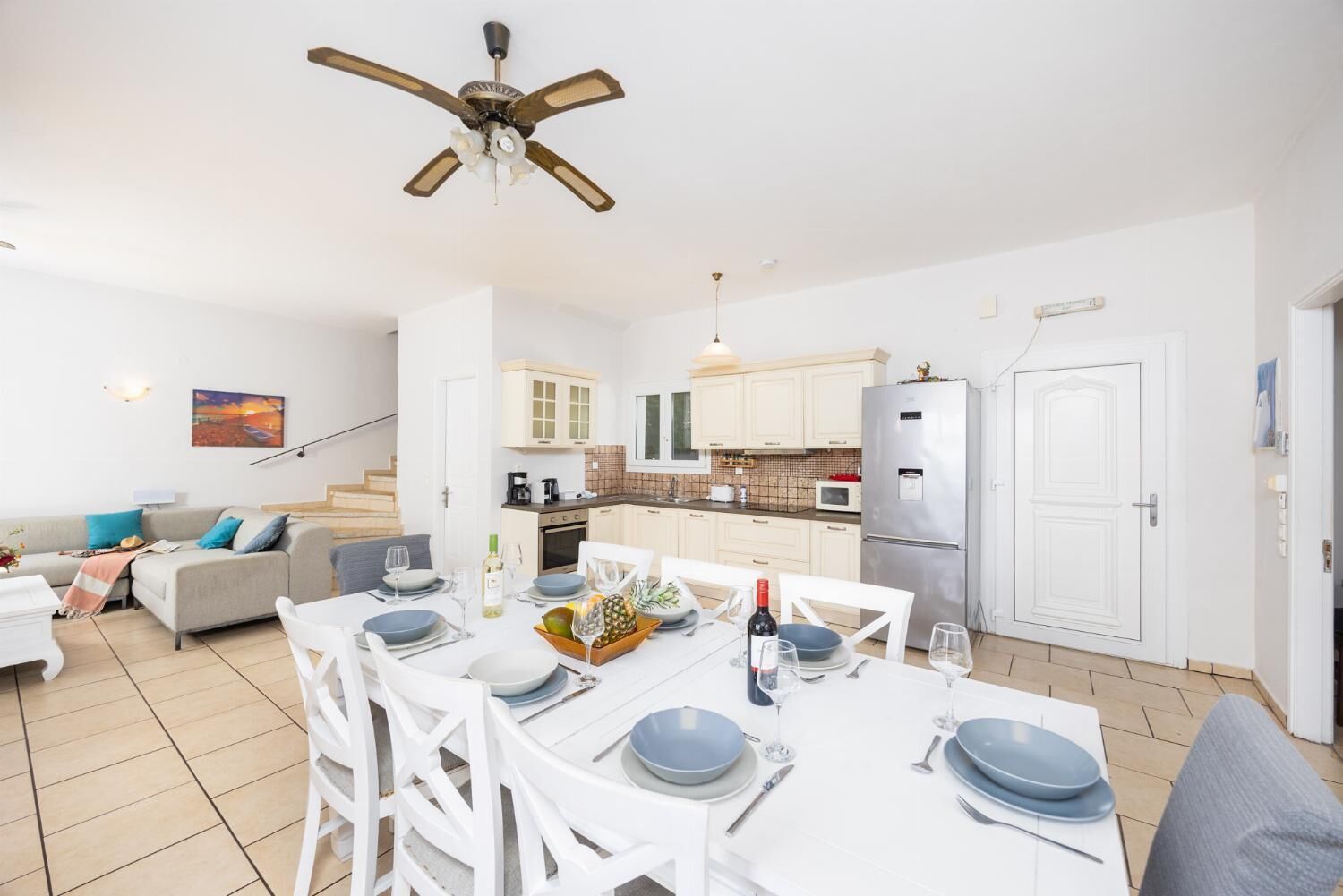 A modern kitchen with white cabinets, a stainless steel refrigerator, and a dining area with a white table set for six.