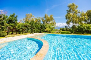 A swimming pool with a curved edge, surrounded by trees and a clear sky. - Ormos Beach House in Apraos (Corfu)