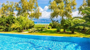 A swimming pool with clear blue water, surrounded by lush greenery and trees. - Ormos Beach House in Apraos (Corfu)