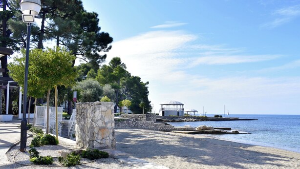 A coastal promenade with stone pathways, a gazebo, and a lighthouse in the distance. - Holiday Home With Garden and BBQ in Umag (Umag)
