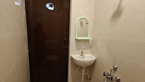 A bathroom with a door, a sink, a shower, and a red bucket. - Hotel Mauris & Restaurant By Wishotel  (Indore)