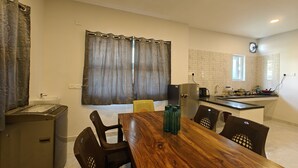 A modern kitchen with a built-in fridge, a sink, and a window. There is a dining table with chairs and a small refrigerator. - Hotel Mauris & Restaurant By Wishotel  (Indore)