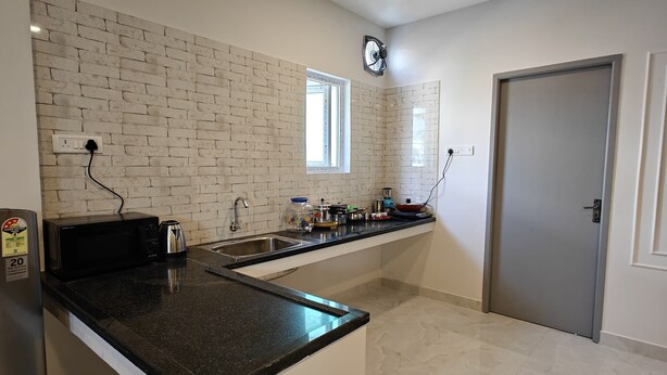 A modern kitchen with a black countertop, white cabinets, and a brick-patterned backsplash. - Hotel Mauris & Restaurant By Wishotel  (Indore)
