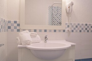 A bathroom with a white sink, a mirror, and a hairdryer mounted on the wall. - A sophisticated space designed to accommodate up to four people, where comfort and style meet. The living room features a comfortable double sofa bed, while the bedroom, equipped with a double bed, offers an intimate and relaxing atmosphere. The modern b (Costa Serena)
