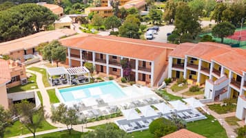 Un complejo turístico con piscina central, varias habitaciones para huéspedes y una cancha de tenis.