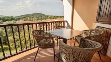 Un balcón con una mesa y cuatro sillas de mimbre, con vistas a un paisaje pintoresco con colinas y árboles.