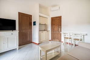 A compact living space with a kitchenette, a flat-screen TV, a dining table, and a sofa.