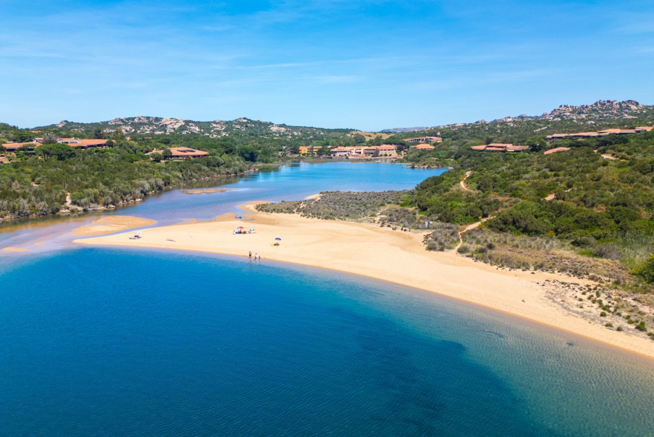 Eine Küstenlandschaft mit sandigem Strand, klarem, blauem Wasser und umgebender Vegetation.