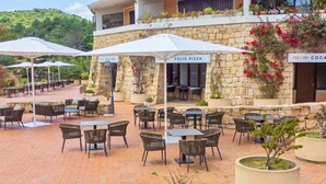 An outdoor patio area with stone walls, wicker furniture, and umbrellas. - A sophisticated space designed to accommodate up to four people, where comfort and style meet. The living room features a comfortable double sofa bed, while the bedroom, equipped with a double bed, offers an intimate and relaxing atmosphere. The modern b (Costa Serena)