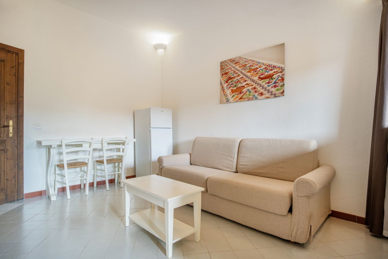 A living room with a beige sofa, a white coffee table, and a dining area with white chairs and a small table.