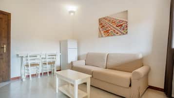 A living room with a beige sofa, a white coffee table, and a dining area with white chairs and a small table.