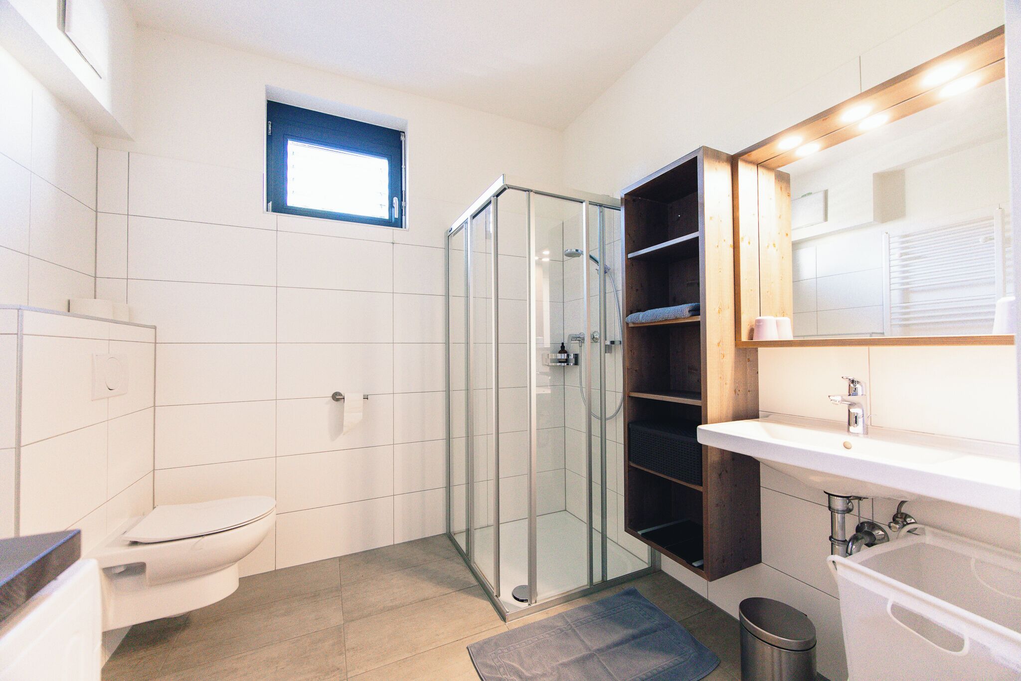 Une salle de bain moderne avec une douche à parois de verre, des toilettes blanches et un lavabo avec un meuble-vasque en bois.