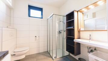 Une salle de bain moderne avec une douche à parois de verre, des toilettes blanches et un lavabo avec un meuble-vasque en bois.