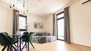 A modern living room with a dining area, featuring a sofa, green chairs, a small table, and a large window with curtains. - GH Luxury Apartments Graz, Kalvarienberg (Graz)