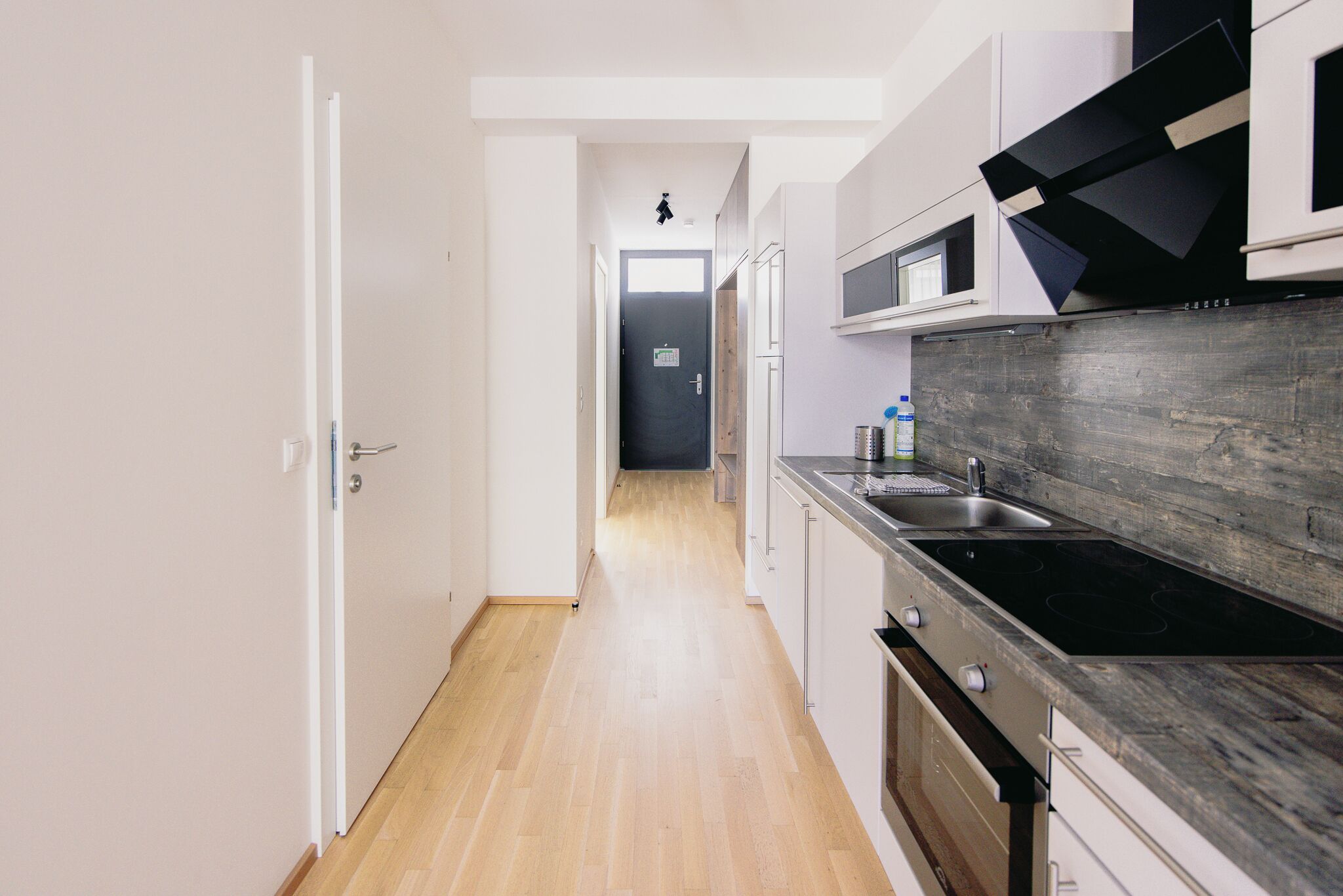 Een moderne keuken met een houten vloer, witte kasten, een zwart fornuis en een magnetron.