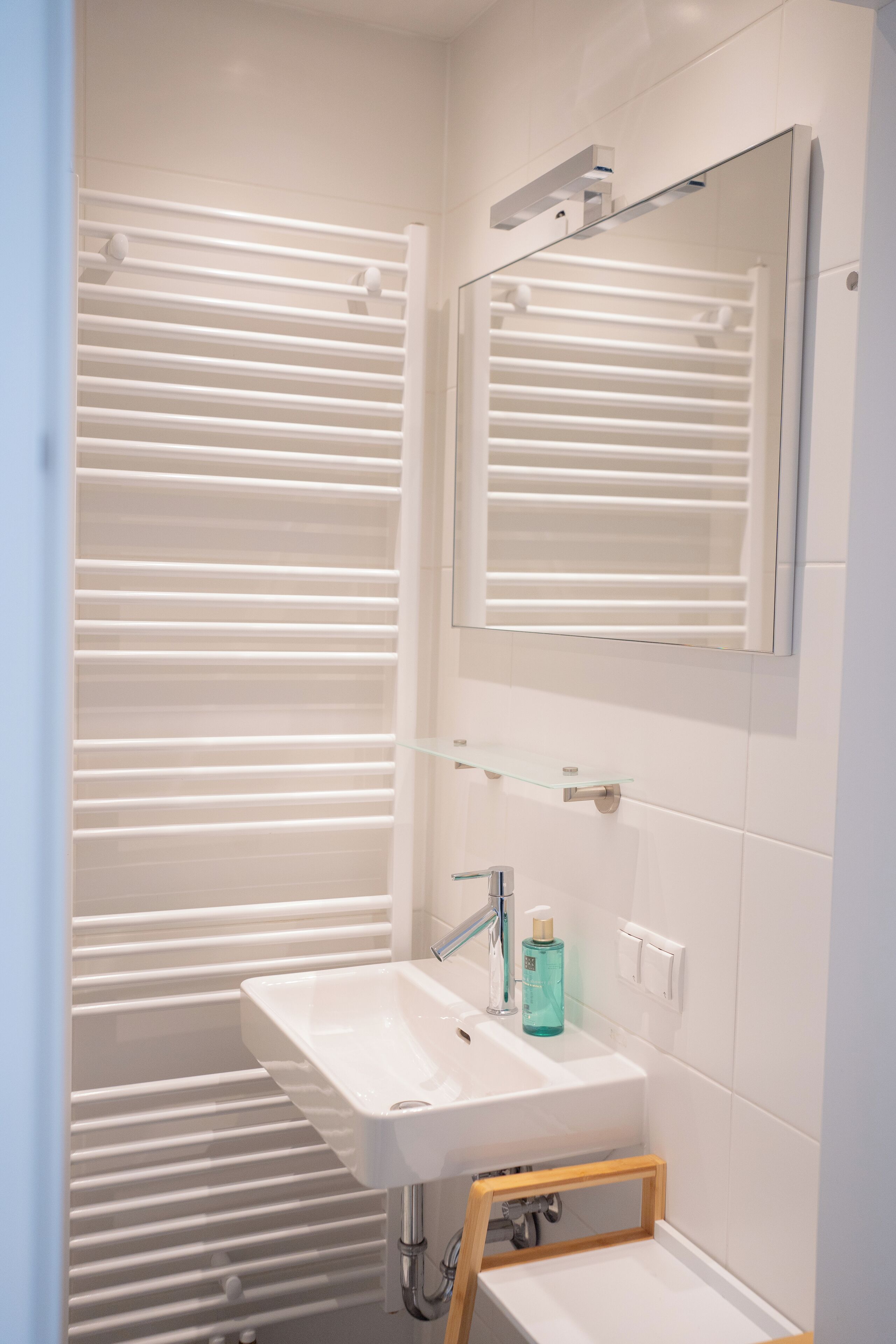 Un bagno moderno con un lavandino bianco, uno specchio e una mensola in vetro.