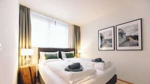 A hotel room with a large bed, two bedside tables, a window with curtains, and two framed pictures on the wall. - GH Luxury Apartments Graz, Kalvarienberg (Graz)